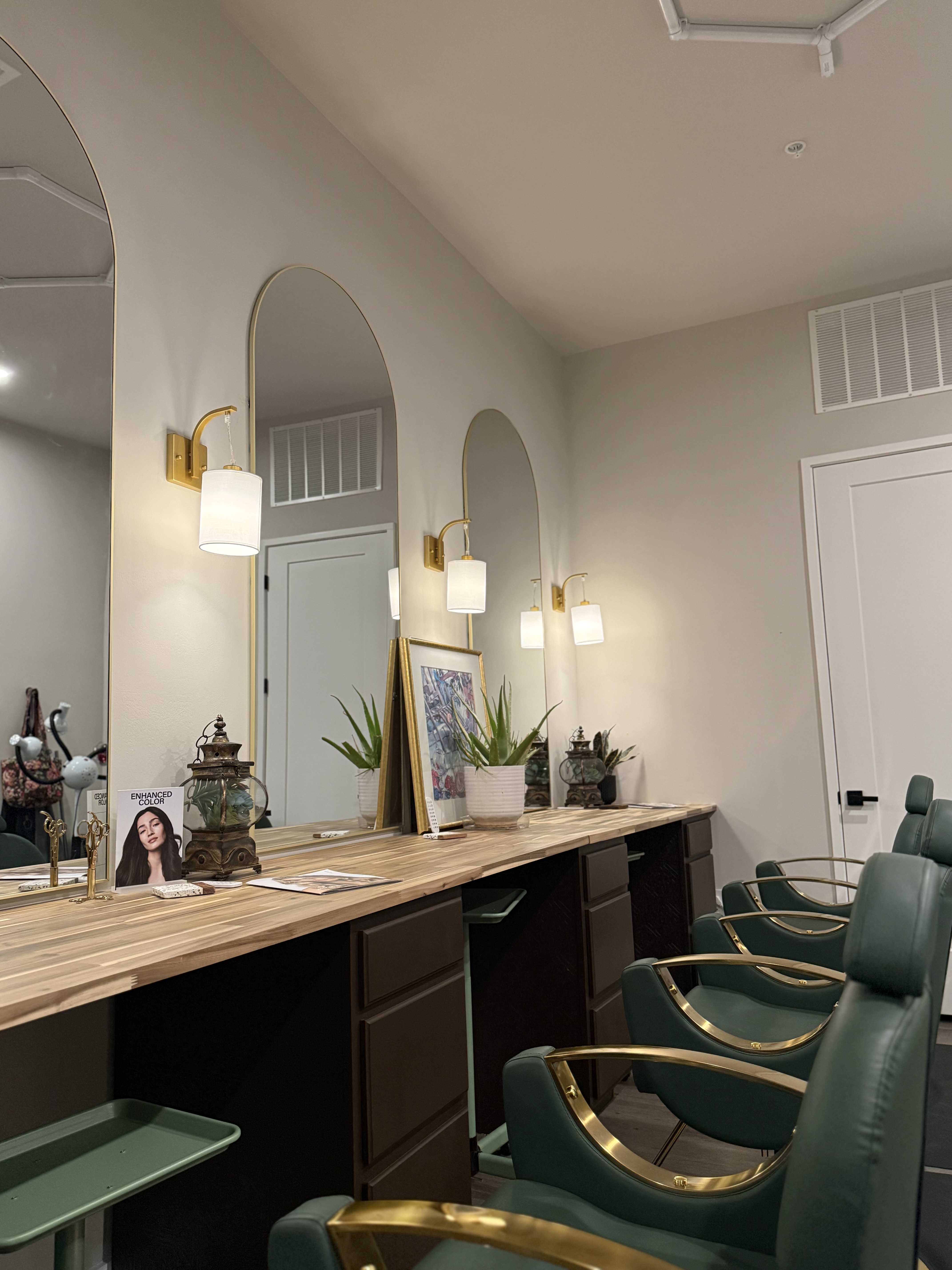 Grand Collective salon stations with green chairs, arched mirrors, and warm lighting